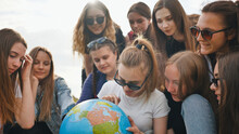 A Group Of Cheerful Girls Is Exploring The Globe Of The World In The Meadow.