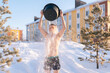 Leinwandbild Motiv Front view of young man pouring water from bucket onto his head, tempering his body, developing resistance to cold outdoors, enjoying winter freshness outdoors in frozen sunny day.