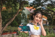 A petite young cosplayer in a sailor crop top uniform takes a selfie with her smartphone. An asian teen taking a snapshot. Outdoor scene.