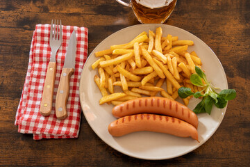 top view of a plate of fries with frankfurters on a table with a beer