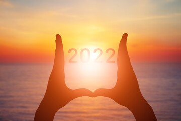 Poster - 2022 is supported by hands on the background of a sunny sunset.