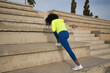 © Manuel - African-American woman with afro hair and sportswear, with fluorescent yellow sweatshirt and leggings, doing leg stretches on stairs. Fitness concept, sport, street, urban.