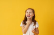 cute smiling preschool girl holds her first fallen baby tooth in her hand while standing on yellow background. growing permanent tooth is in the open mouth. . The concept of hygiene of baby teeth.