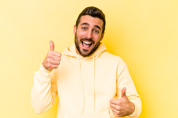 Young caucasian man isolated on yellow background raising both thumbs up, smiling and confident.