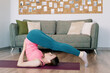 © arthurhidden - Attractive woman practicing yoga at home on a green sofa background