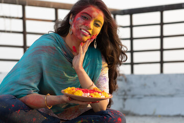 Wall Mural - Pretty Young indian smart girl sitting relaxing and enjoying with face coloured with gulal for festival of colours Holi, a popular hindu festival celebrated across india