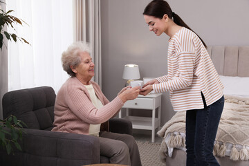 Wall Mural - Young caregiver giving tea to senior woman in room. Home care service