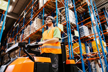 A warehouse worker with voice picking headset driving forklift.