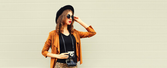 Portrait of stylish young woman photographer with film camera on gray background