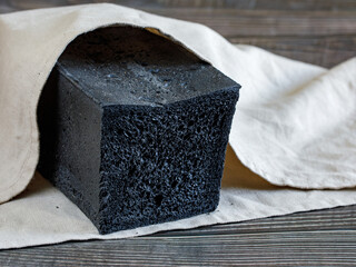 Black coal toast bread on a wooden table with a gray napkin, chopped, side view, horizontal, selective focus