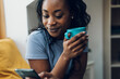 © Zamrznuti tonovi - African american woman sitting on windowsill with a cup of coffee and a smartphone