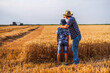 © djoronimo - Farmers are standing in their wheat field while the harvesting is taking place. Father is teaching his son about agriculture.