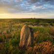 Beautiful evening landscape in the steppe meadow. Blue sky with clouds and sunlight. Granite rock, feather grass in the foreground.