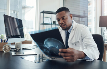 Poster - Examining this scan for any injuries. Shot of a young doctor examining an x-ray in an office.