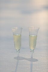 Two glasses of champagne are standing in a snowdrift in the contoured sunlight