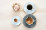Group of cups with various coffee, espresso, cappuccino, lungo black and with crema on a light wooden table, copy space, high angle view from above,