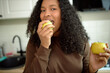 © Anatoliy Karlyuk - Close-up of pretty African female of 20s biting yellow-green apple and holding another one in other hand, looking at camera, posing against kitchen background. Healthy food. Strong teeth