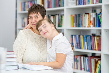 Poster - Portrait of a happy senior woman and smiling girl with syndrome down at library. Education for disabled children concept