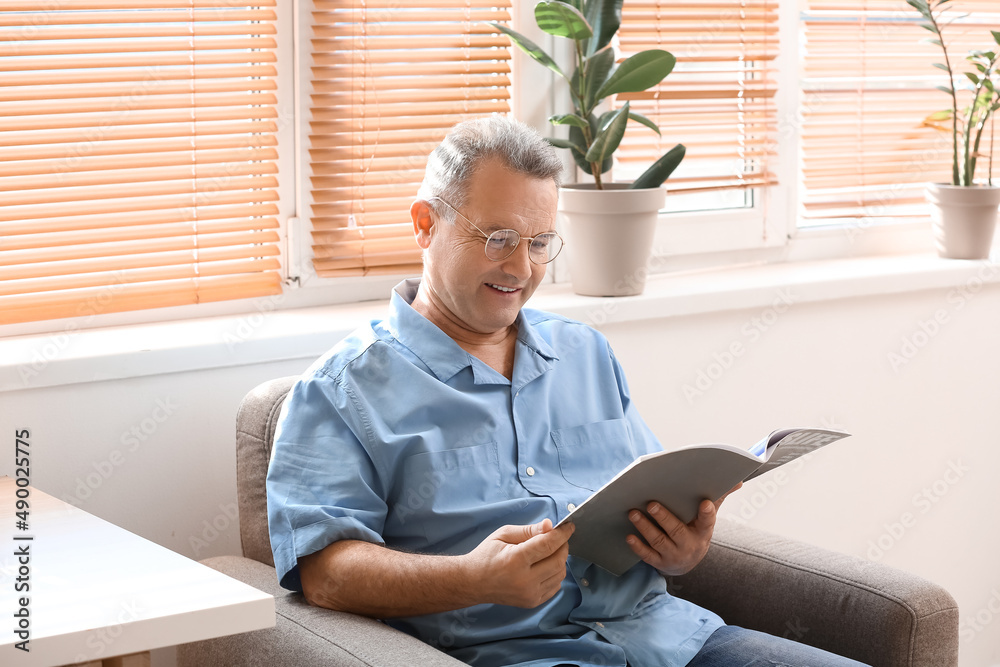 Senior man in eyeglasses reading magazine at home