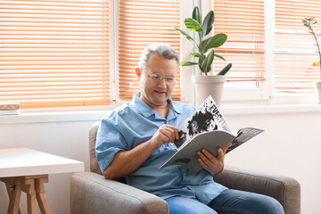 Wall Mural - Senior man in eyeglasses reading magazine at home