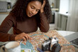 © Anatoliy Karlyuk - Close-up picture of gorgeous charming tender girl tourist of 20s with dark skin in brown sweater studying city road map before going for walk visiting new place, vintage camera lying next to her