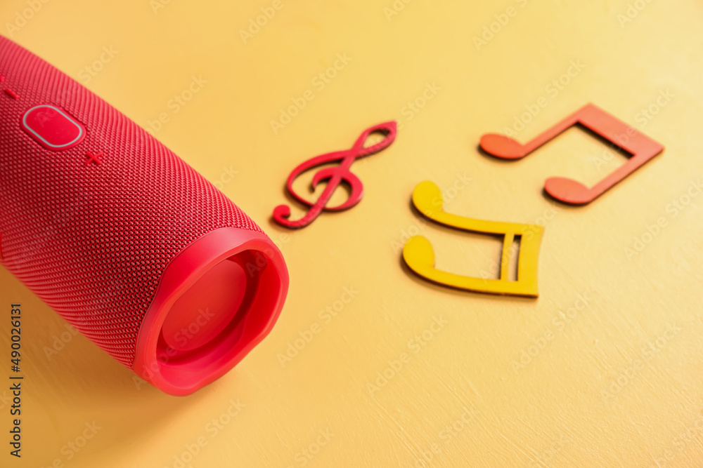 Wireless portable speaker and music notes on color background, closeup