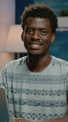 Poster - Close up of african american man working on laptop. Black employee doing remote work on internet while looking at camera and smiling. Business person of african ethnicity using device
