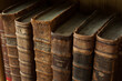 Dusty, worn and faded, leather-bound, large volume, antique Jewish holy books stacked upright on a library shelf.