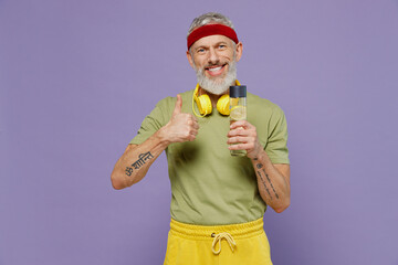 Wall Mural - Excited elderly gray-haired bearded man 40s years old in headband khaki t-shirt hold bottle of water drink show thumb up like gesture isolated on plain pastel light purple background studio portrait.