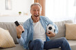 © Prostock-studio - Excited mature man watching tv celebrating goal holding ball