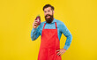 Happy man in red apron holding eggplant yellow background, grocer