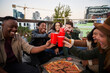 © StratfordProductions - Group of diverse friends making a toast with red cups while sitting on rooftop terrace in the city. Good times and happiness