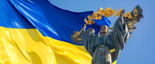 Monument Of Independence Of Ukraine In Front Of The Ukrainian Flag. The Monument Is Located In The Center Of Kiev On Independence Square. Russian War In Ukraine. Stop War.