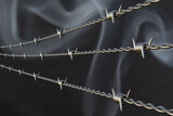 Barbed wire against the background of puffs of gray smoke as a concept of tension between countries, war and economic sanctions