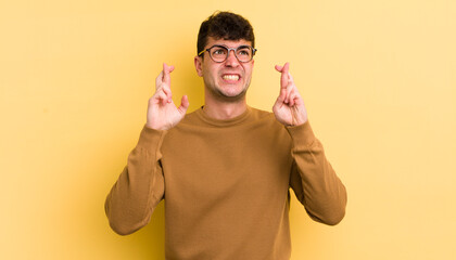 Wall Mural - young handsome man crossing fingers anxiously and hoping for good luck with a worried look