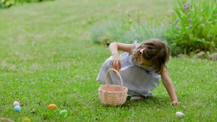 Wall Mural - Girl find and pick up multicolored egg on Easter egg hunt in garden