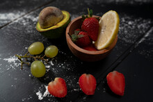 Natural Fresh Red Strawberries And Half Avocado And Green Grapes On Black Background With Lemon Slice