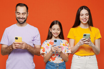 Wall Mural - Young fun parents mom dad with child kid daughter teen girl in basic t-shirts hold in hand use mobile cell phone isolated on yellow background studio portrait Family day parenthood childhood concept