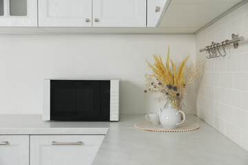 Modern microwave oven, dry flowers, cup and teapot on countertop in kitchen