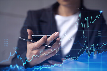 Wall Mural - A woman trader holding in the hands a smart phone and researching stock market to proceed right investment solutions. Internet trading and wealth management concept. Hologram Forex chart.