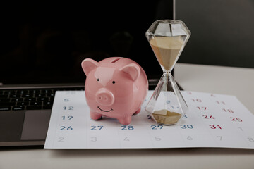 Hourglass with piggy bank on a calendar with laptop