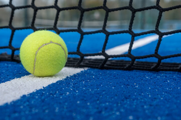 Poster - Yellow ball on floor behind paddle net in blue court outdoors. Padel tennis