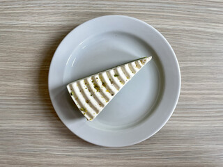 Wall Mural - Top view of piece of delicious pistachio cake with whipped cream on a white plate on a wooden table