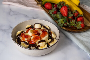 Wall Mural - Closeup of bananas with chocolate glaze and strawberry sauce in a bowl