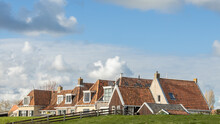 Houses With Red Rooftiles Behind A Dike And Under Blue Sky In Fishermans Village Makkum In The Netherlands