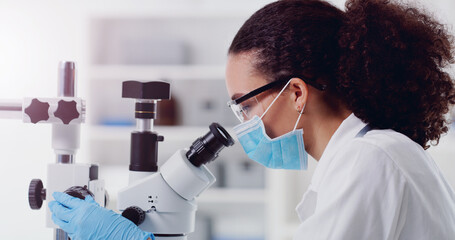 Wall Mural - the solution must be here somewhere. shot of a young scientist using a microscope in a lab.