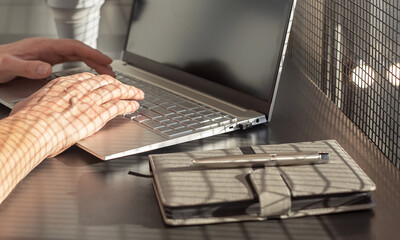 Poster - Man hands closeup typing on laptop keyboard. Businessman sitting at office or home desk with diary and silicon mug and writing text or mail on computer. High quality photo