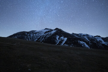 Wall Mural - scenic view of a field against a snowy mountain under the starry night sky