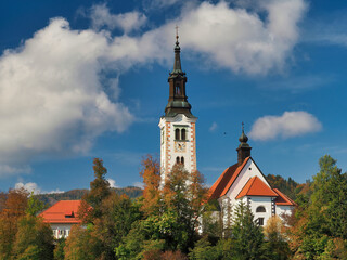 Sticker - Scenic view of a church tower surrounded by green trees under a blue cloudy sky in Slovenia