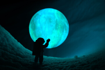 Wall Mural - silhouette of the toy of astronaut against levitating glowing sphere over surface icy planet covered